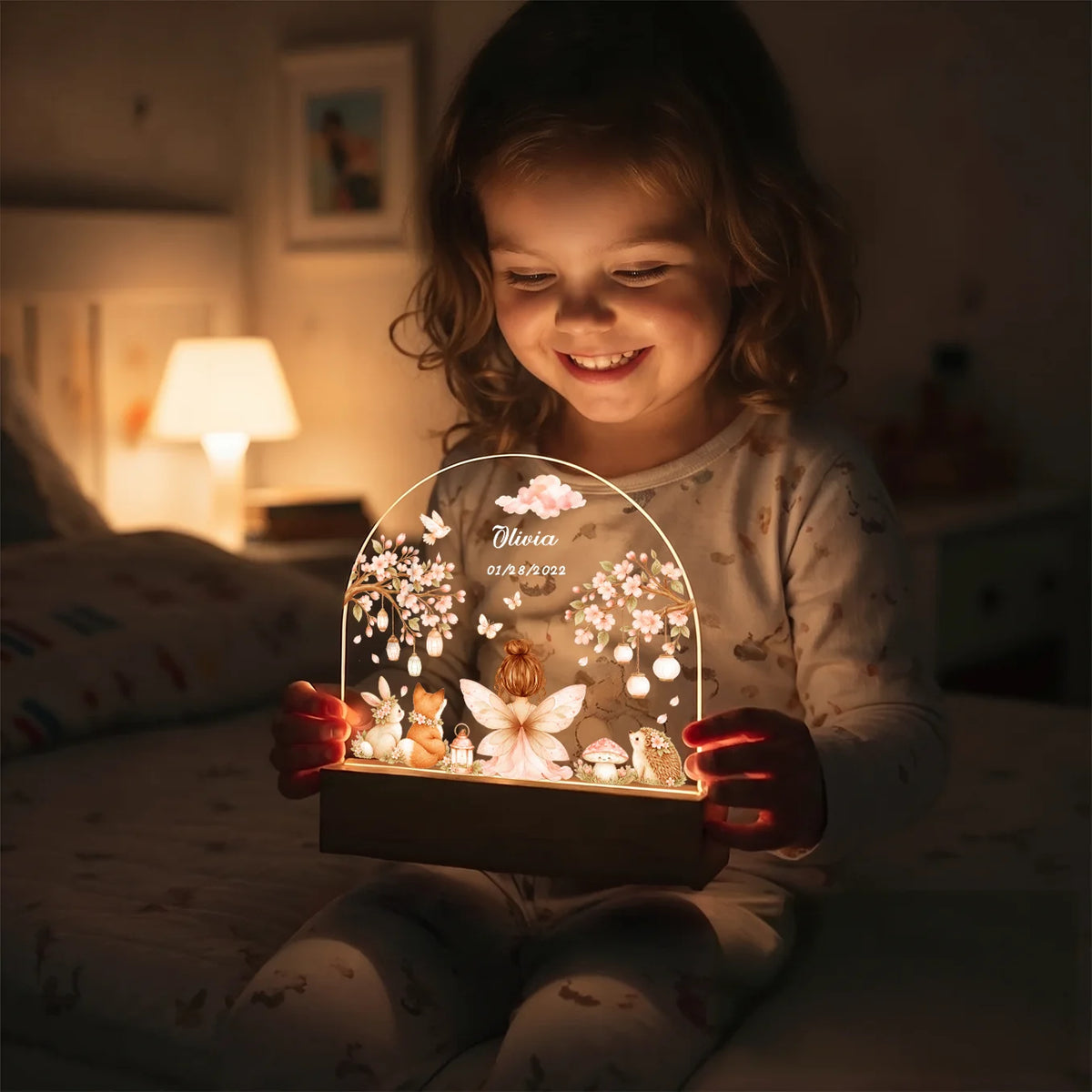 Smiling girl in pajamas holds the glowing Fairy night light with her name
