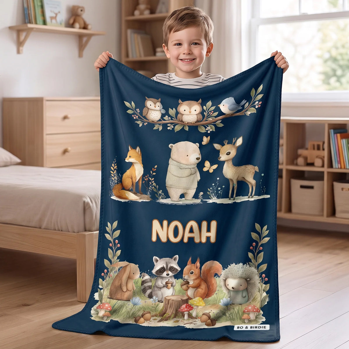 Personalized blanket "Woodland Animals" as a gift for kids: boy holding up a navy fleece blanket with watercolor forest animals and the name Noah, Bo & Birdie