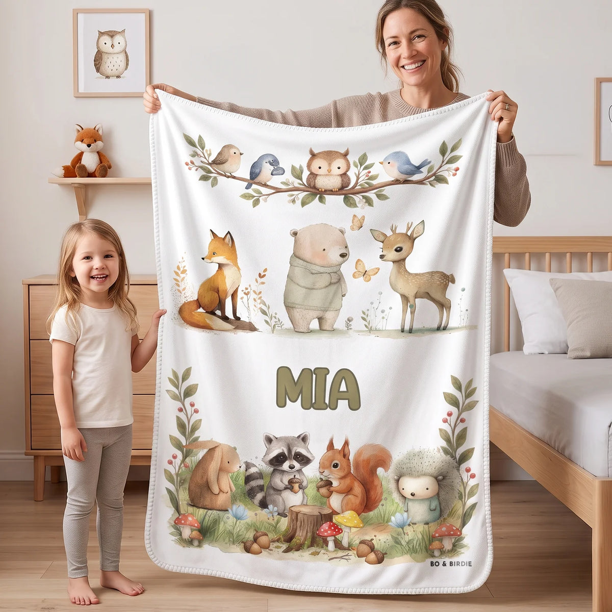 Mom and daughter holding up the white Woodland Animals blanket with the name Mia