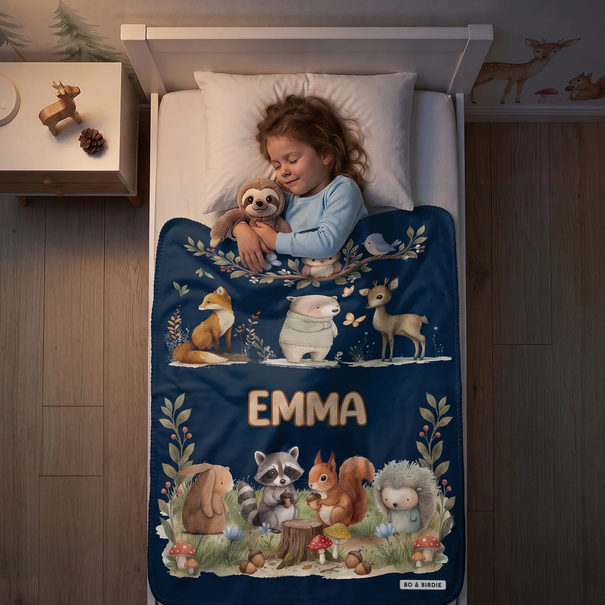 Girl sleeping with a plush toy under the navy Woodland Animals blanket with the name Emma