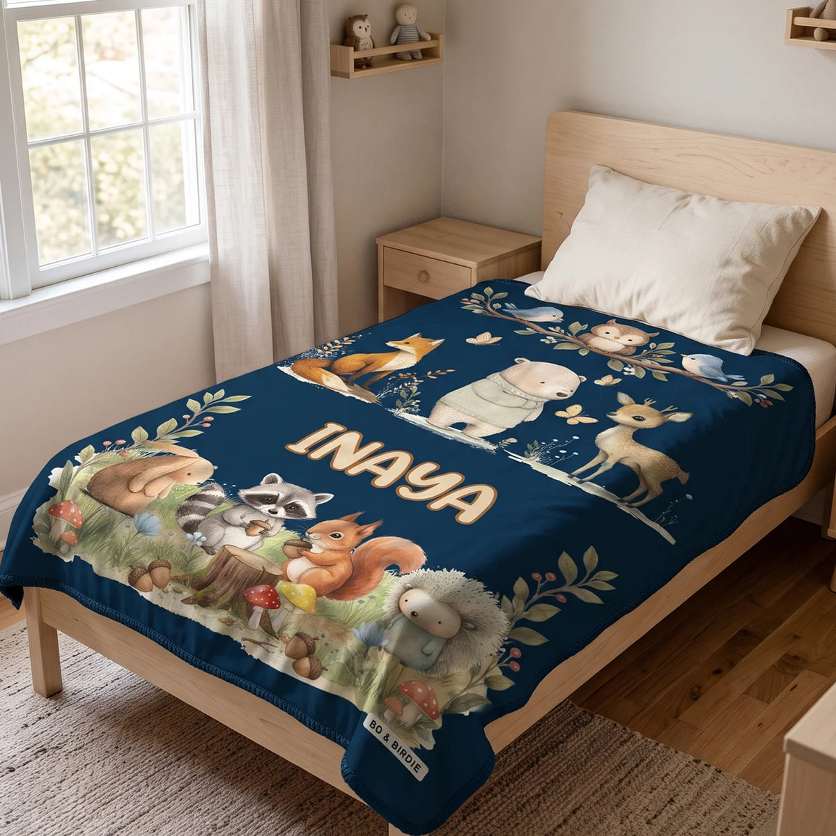 Navy Woodland Animals blanket with the name Inaya spread on a kids bed